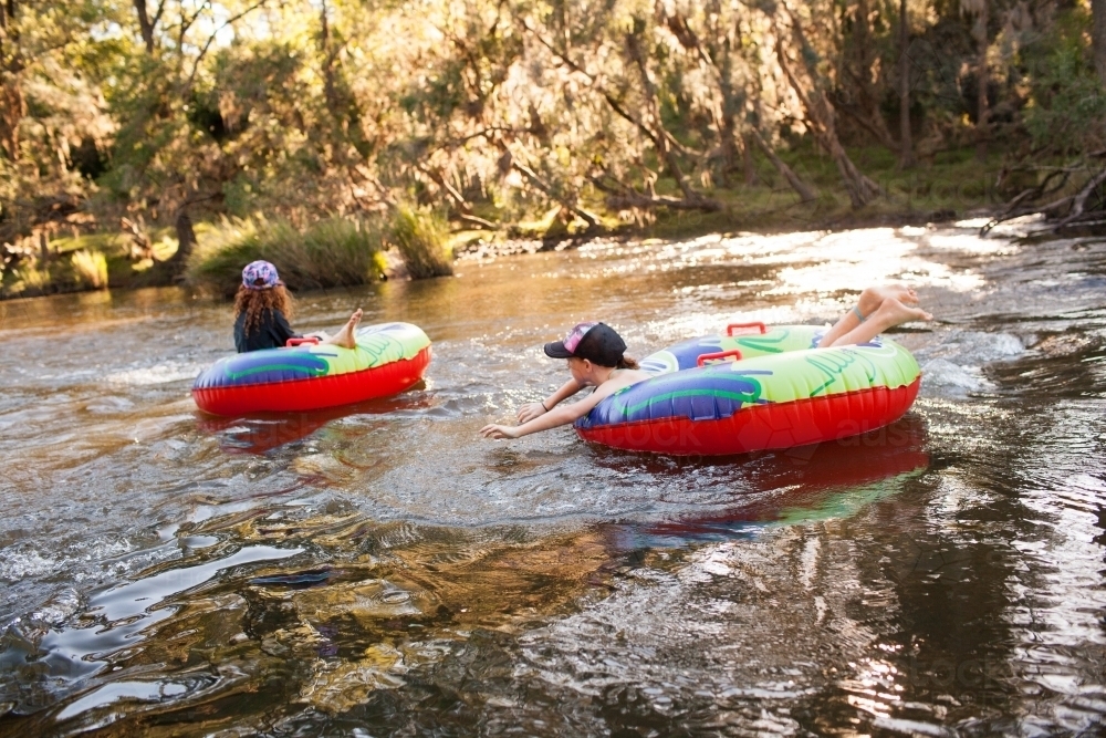 Two girls playing on inflatable rings on a river - Australian Stock Image
