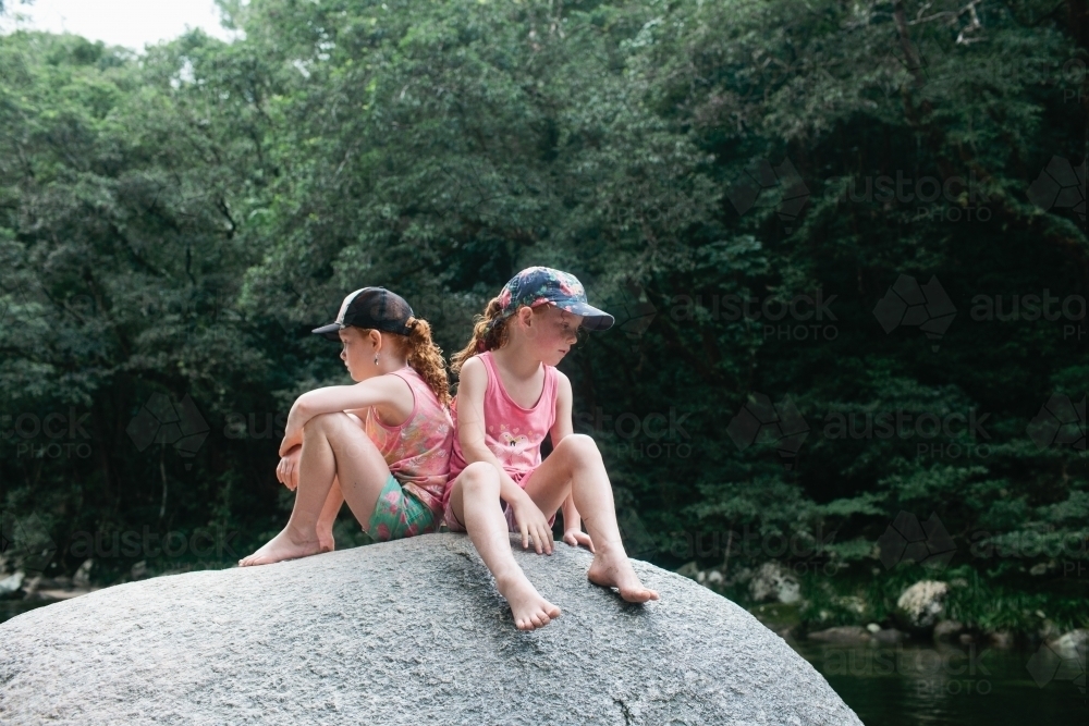 Two girls sitting back to back on a large rock - Australian Stock Image