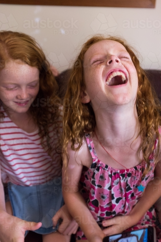 Two girls sitting on a couch laughing together - Australian Stock Image