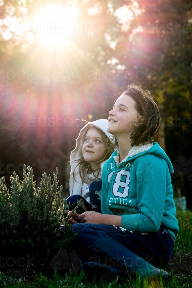 Two girls sitting on grass enjoying the morning sunshine in rural environment - Australian Stock Image
