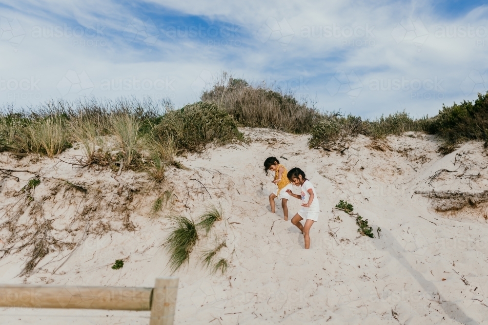 two girls sliding down sand dunes at the beach - Australian Stock Image