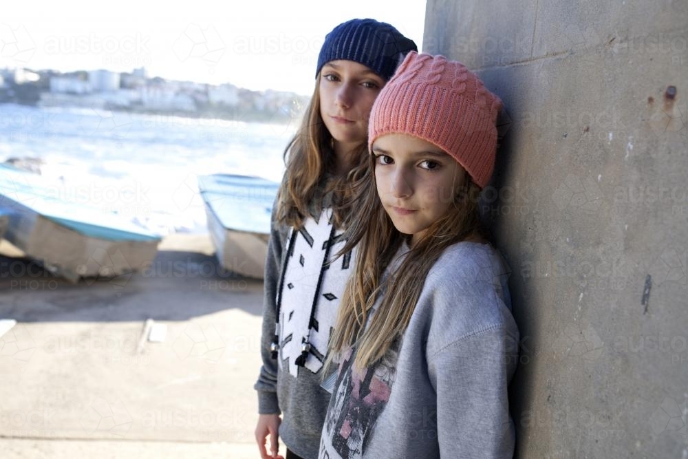 Two girls standing against brick wall posing by the ocean - Australian Stock Image