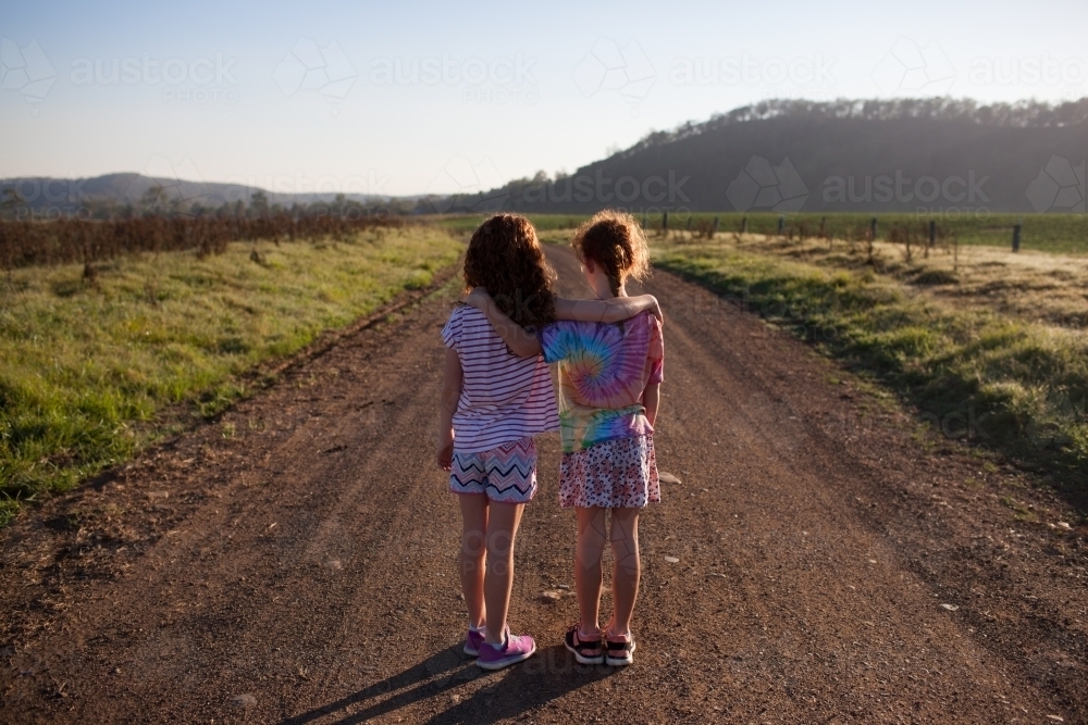 Two girls standing on a dirt road with arms around each other - Australian Stock Image