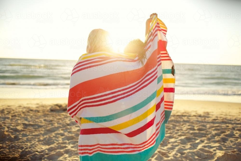 Two girls standing on the beach sharing a beach towel - Australian Stock Image