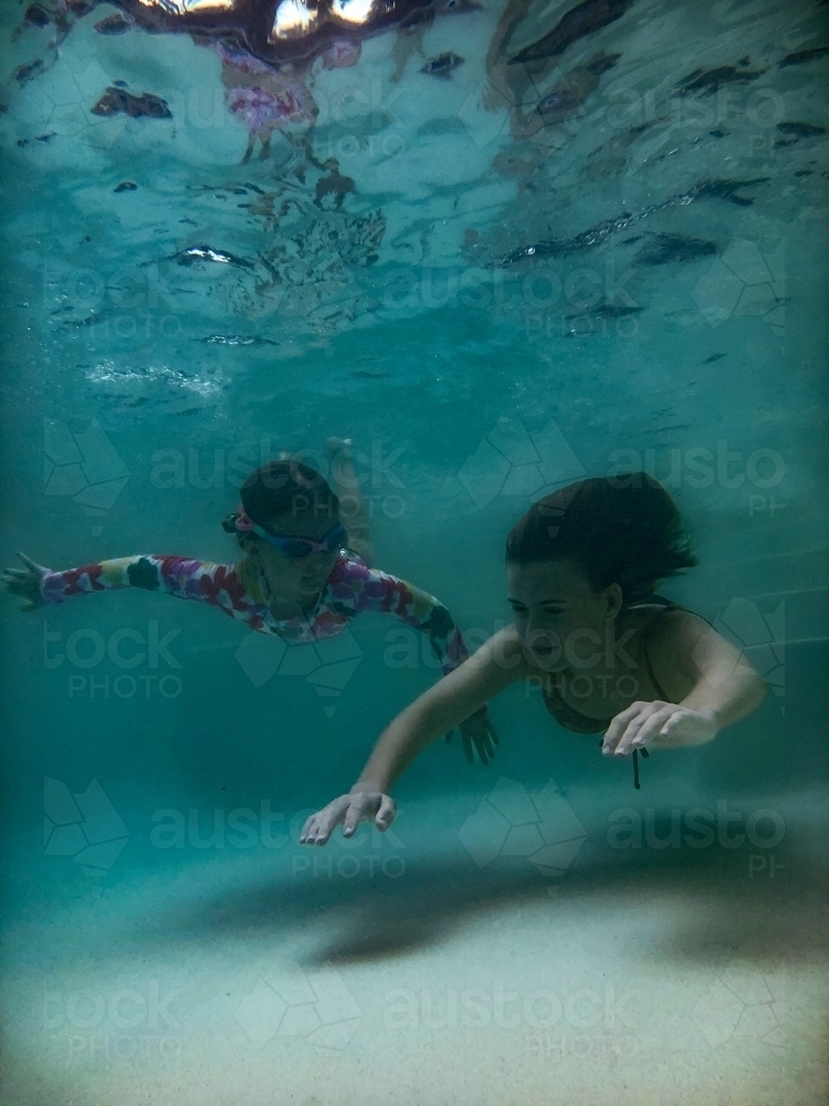 Two girls swimming towards camera underwater in a pool - Australian Stock Image