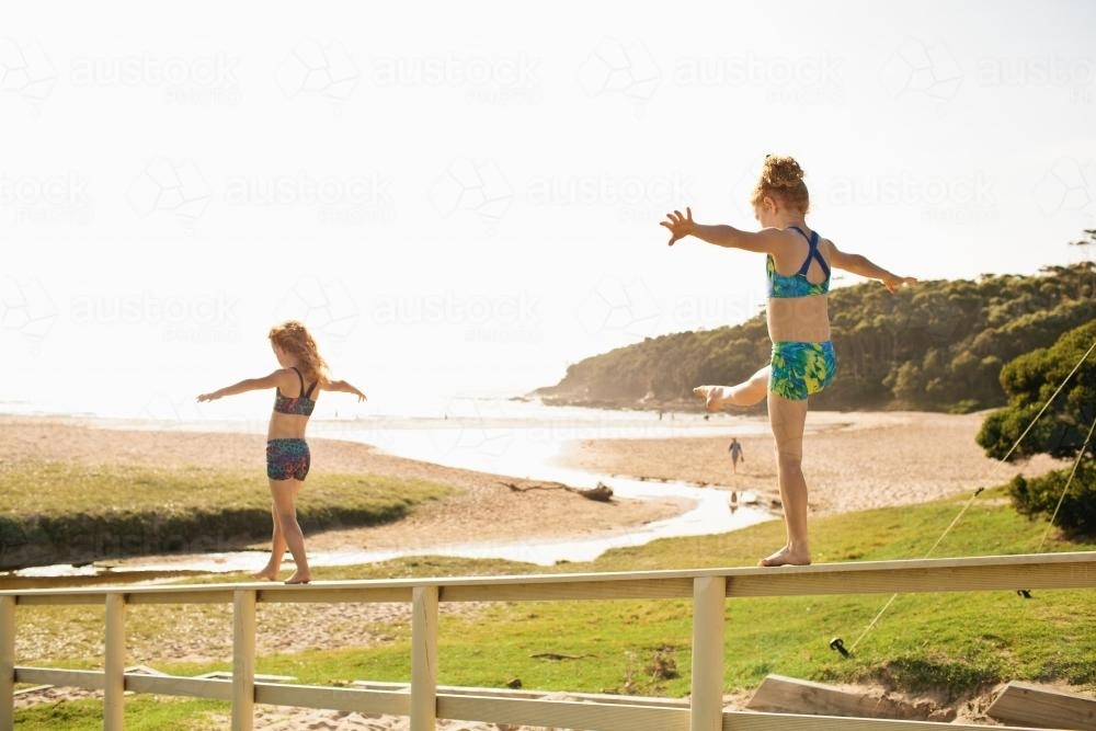 Two girls walking along a fence railing at the beach - Australian Stock Image