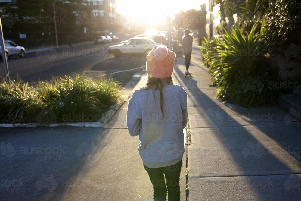 Two girls walking away on a footpath in the afternoon light - Australian Stock Image