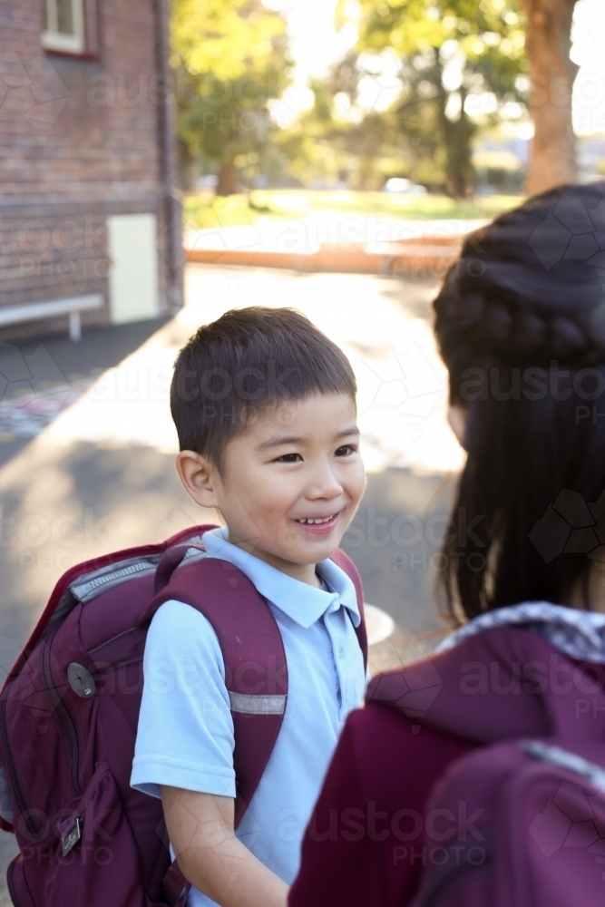 Two happy children talking in the playground as they leave school - Australian Stock Image