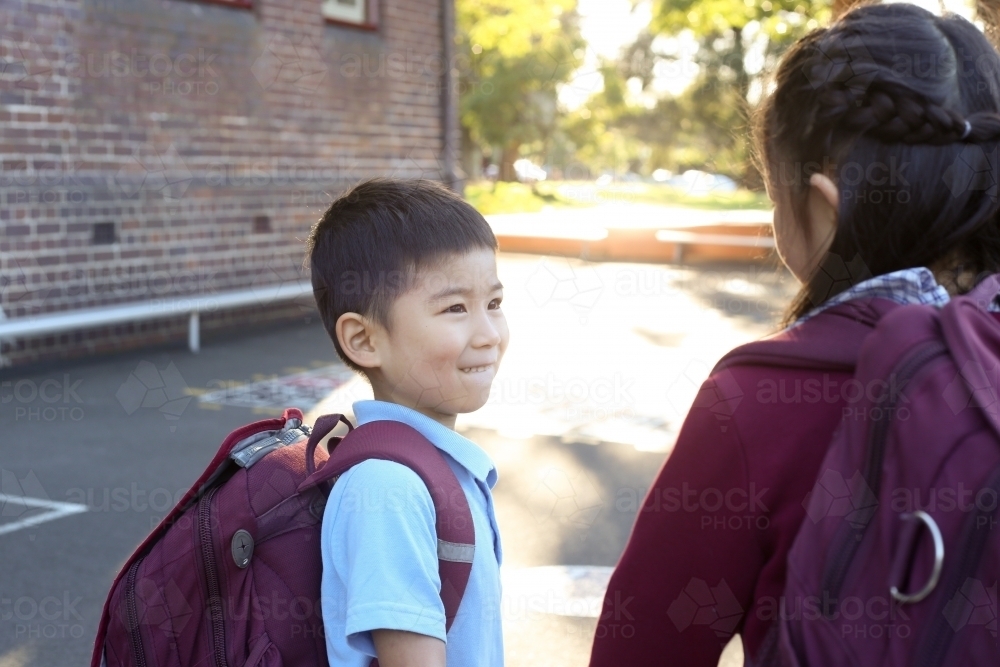 Two happy children talking in the playground as they leave school - Australian Stock Image