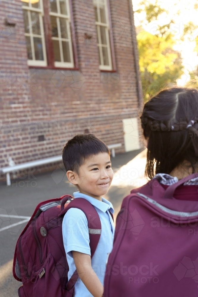 Two happy children talking in the playground as they leave school - Australian Stock Image