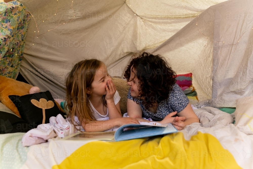 Two happy girls reading a book together in cubby house tent - Australian Stock Image