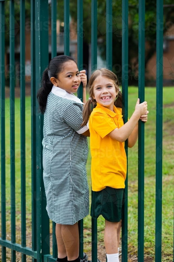 two happy primary school girls swinging off school fence - Australian Stock Image