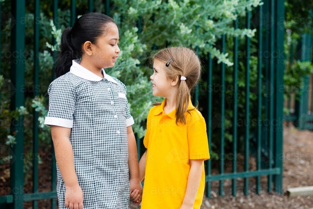 Two happy school friends talking together older girl looking after younger girl - Australian Stock Image