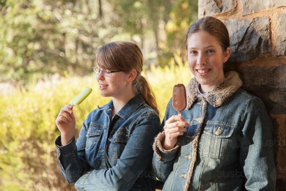 Two happy teenage sisters standing together eating ice blocks in winter - Australian Stock Image