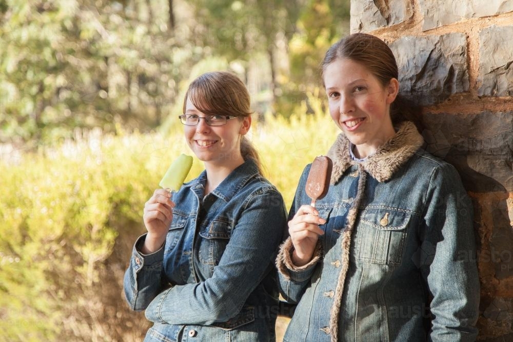 Two happy teenage sisters standing together eating ice blocks in winter - Australian Stock Image