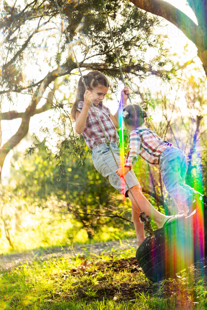 Two happy young Australian children swinging together in front yard of rural home on tyre swing - Australian Stock Image