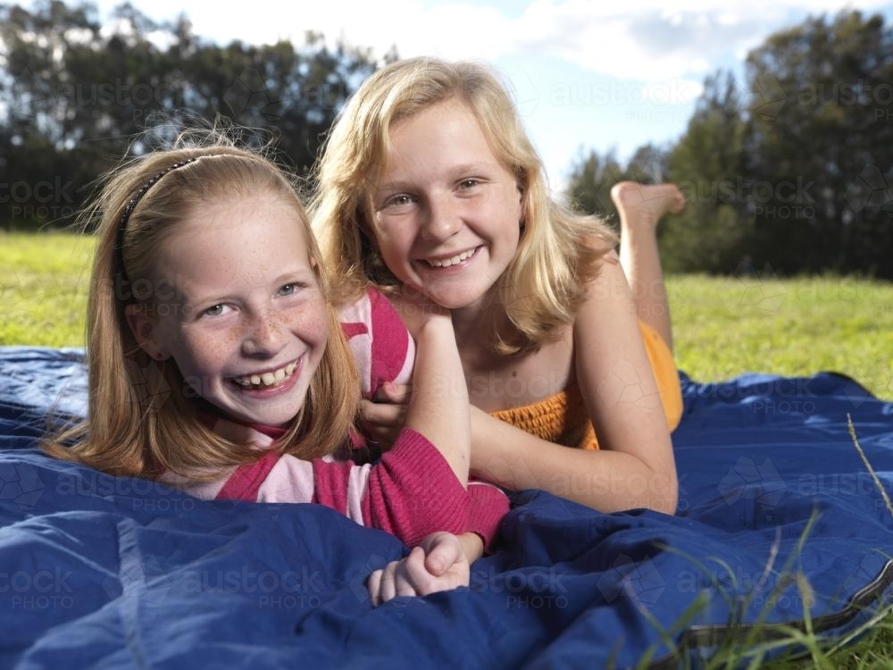 Two happy young girls lying together on the ground - Australian Stock Image