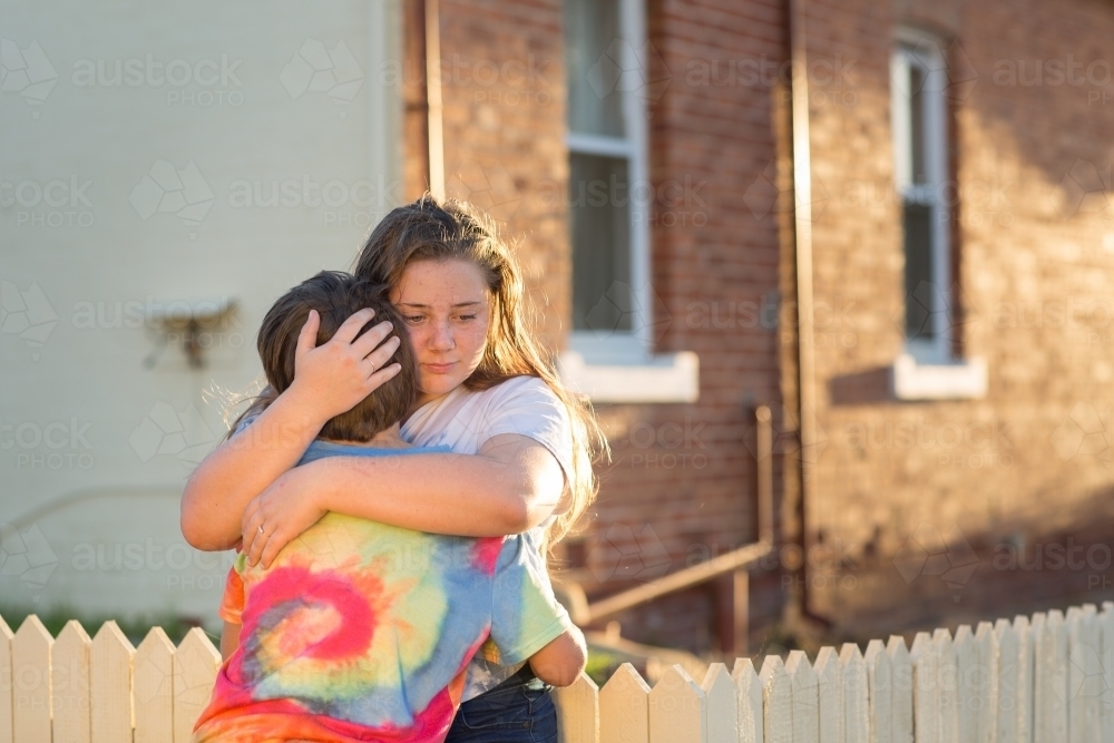 Two kids embracing outside an old house - Australian Stock Image