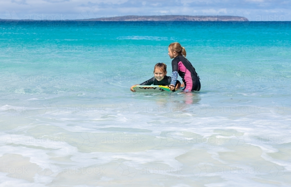 two kids in the water with a boogie board - Australian Stock Image