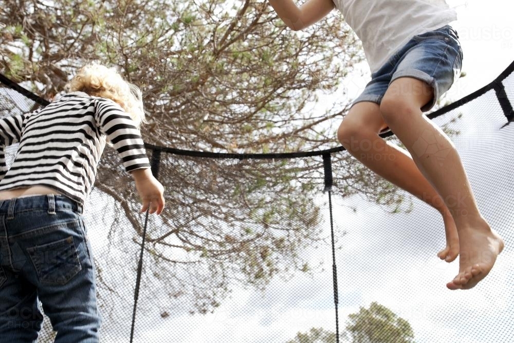 Two kids jumping on trampoline in backyard - Australian Stock Image