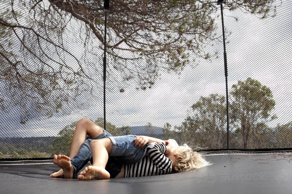 Two kids rolling around wrestling on trampoline in backyard - Australian Stock Image