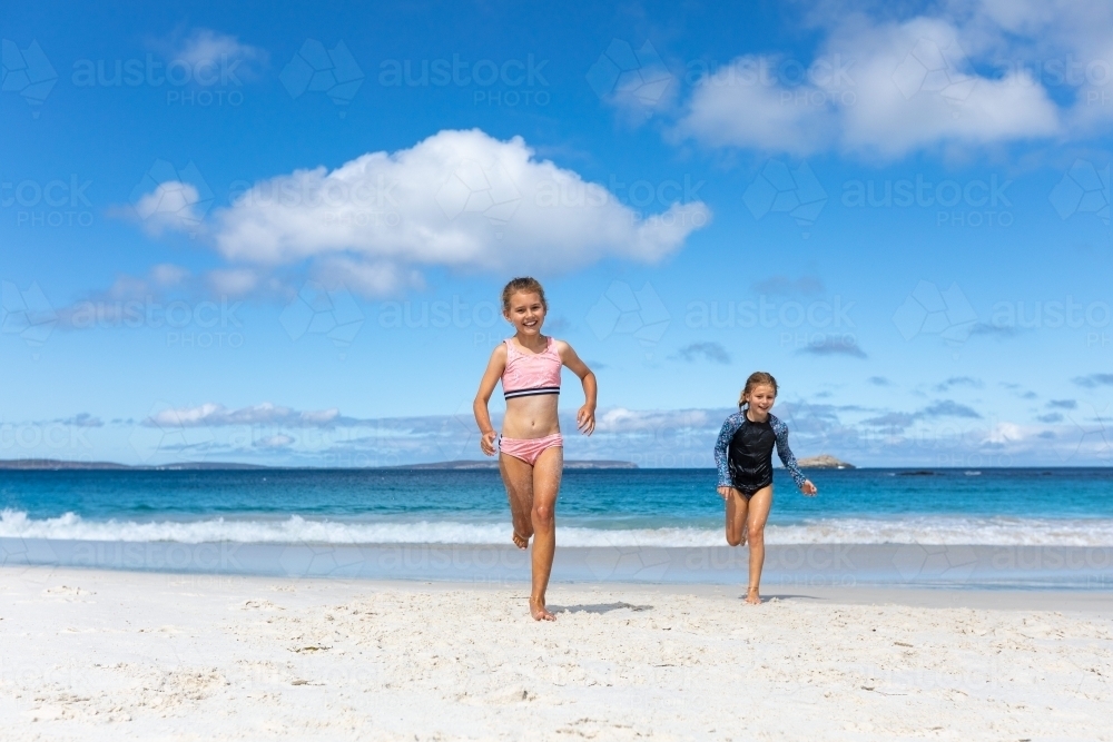 Two kids running up the beach away from the water - Australian Stock Image