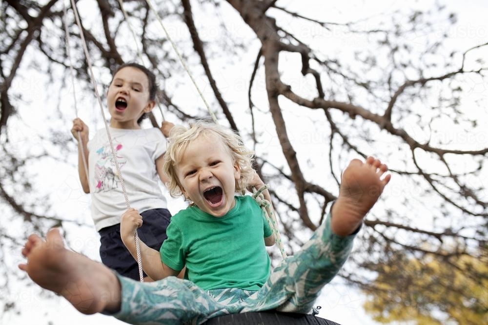 Two kids shouting and swinging on tyre swing - Australian Stock Image