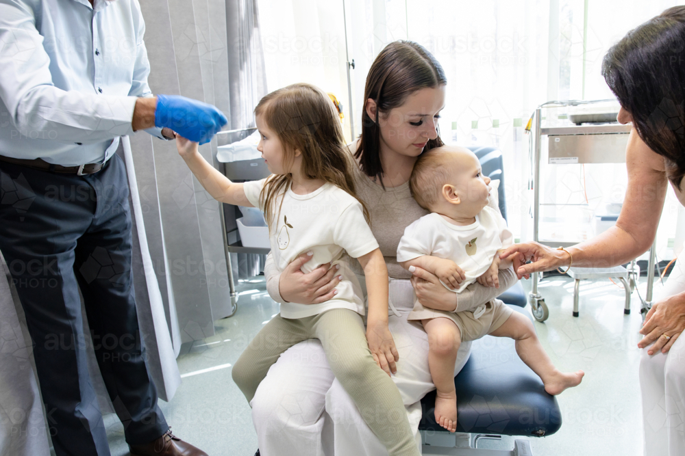 Two kids sitting on mothers lap inside doctors clinic - Australian Stock Image