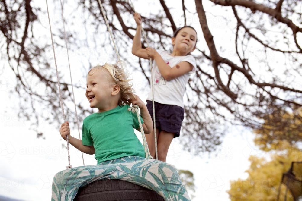 Two kids swinging on tyre swing - Australian Stock Image