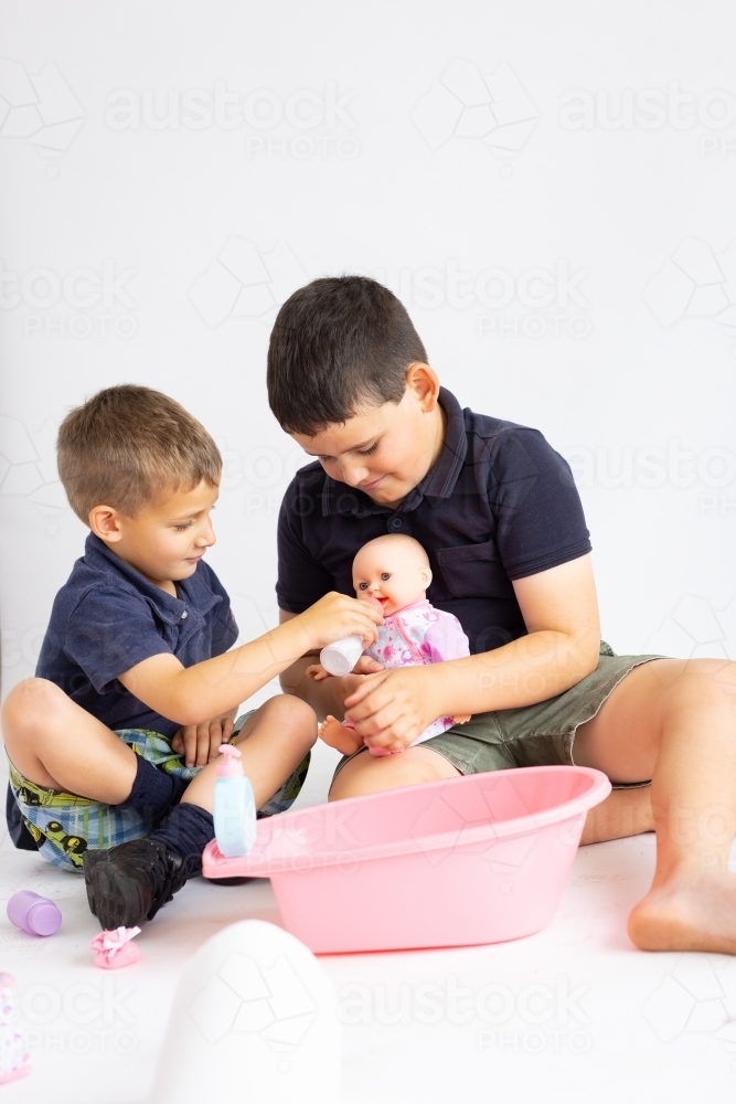 two little boys playing with a baby doll on white background - Australian Stock Image