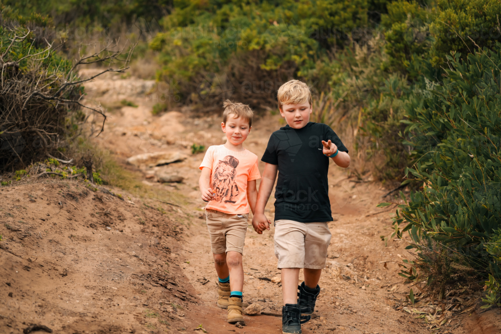 Two little boys walking down beach access track together holding hands - Australian Stock Image