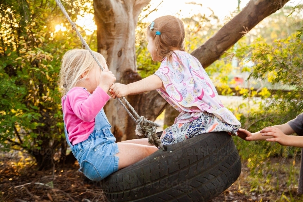 Two little girls on tyre swing in backyard - Australian Stock Image
