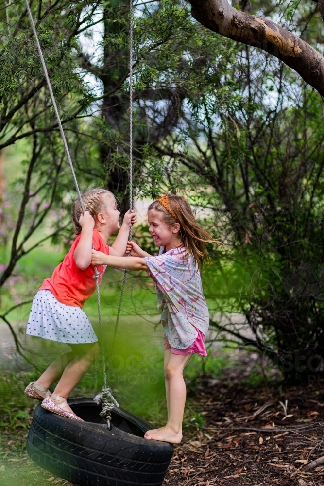 Two little girls playing on a tyre swing on a gum tree in the front yard of a rural property - Australian Stock Image