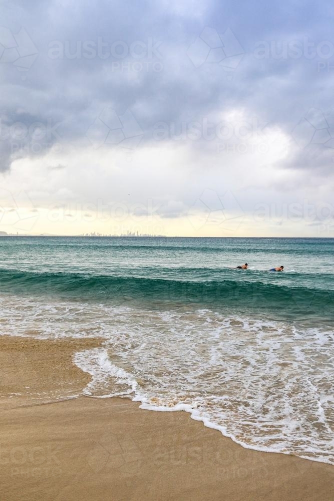 Waves rolling onto a sandy beach at sunrise, with soft morning light reflecting across the water. - Australian Stock Image