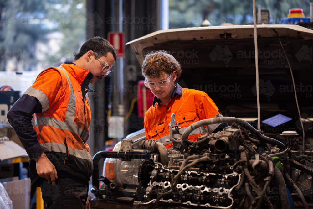 Two male mechanics inspecting vehicles engine in workshop - Australian Stock Image