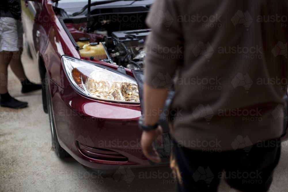 Two mechanics inspect the headlight of a vehicle. - Australian Stock Image