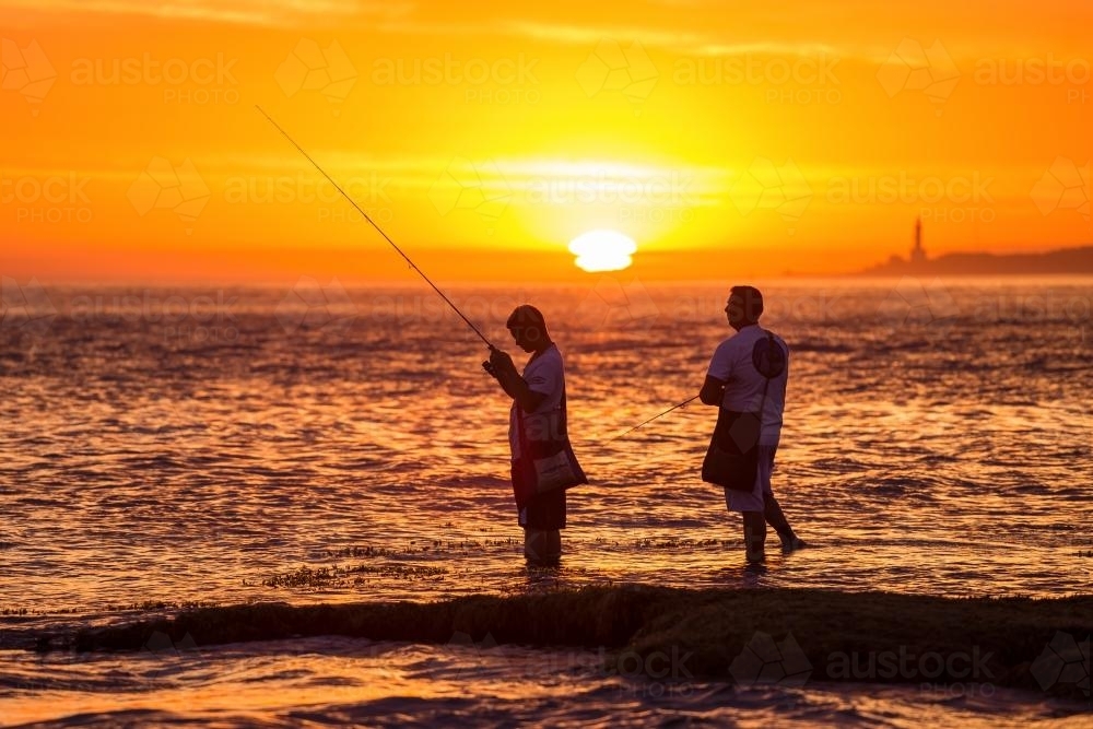 Two men fish off rocks at sunset - Australian Stock Image