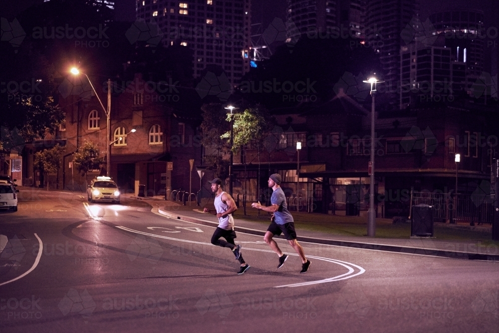 Two men fitness training in urban city at night running - Australian Stock Image