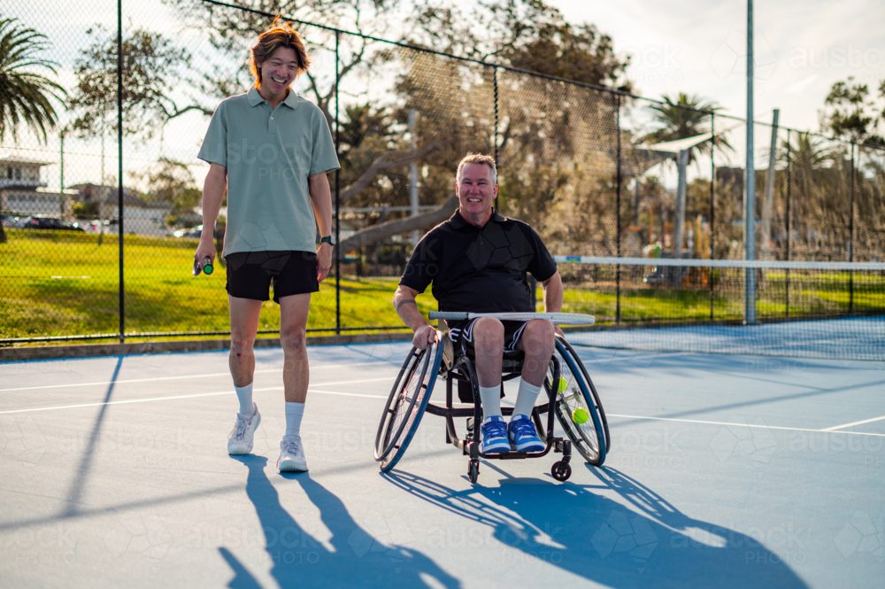 Two men, one in a wheelchair, entering a tennis court in a sunny afternoon - Australian Stock Image