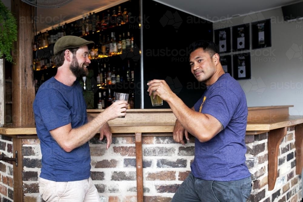 Two men sharing a drink and raising glasses at local craft beer bar - Australian Stock Image