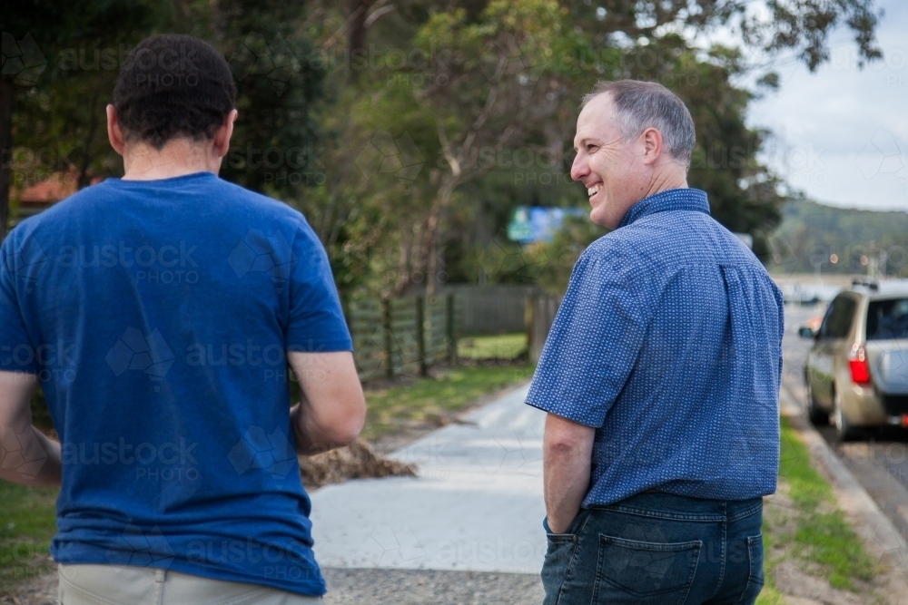 Two men talking to one another as they walk down footpath - Australian Stock Image