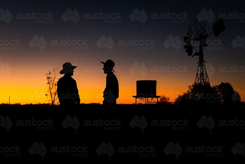 Two men with hats talking under the orange sunset sky - Australian Stock Image