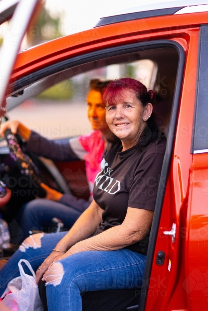 two middle-aged women in red car with passenger door open - Australian Stock Image