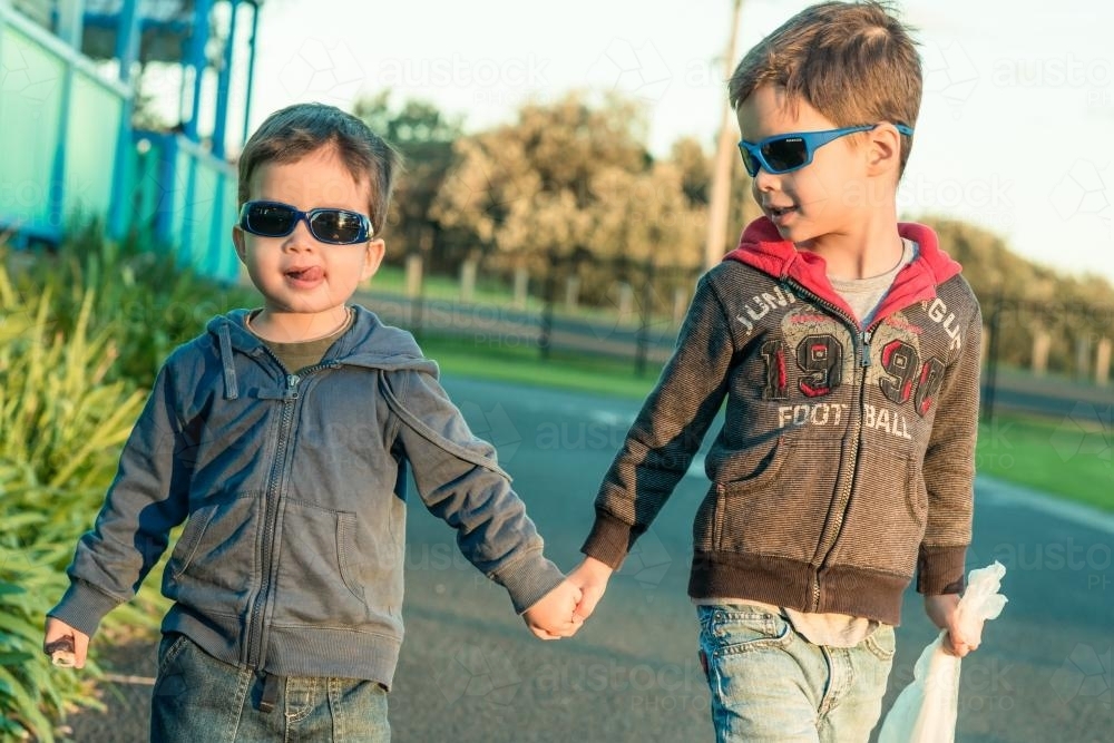 Two mixed race brothers holding hands and walking through a coastal NSW holiday park - Australian Stock Image