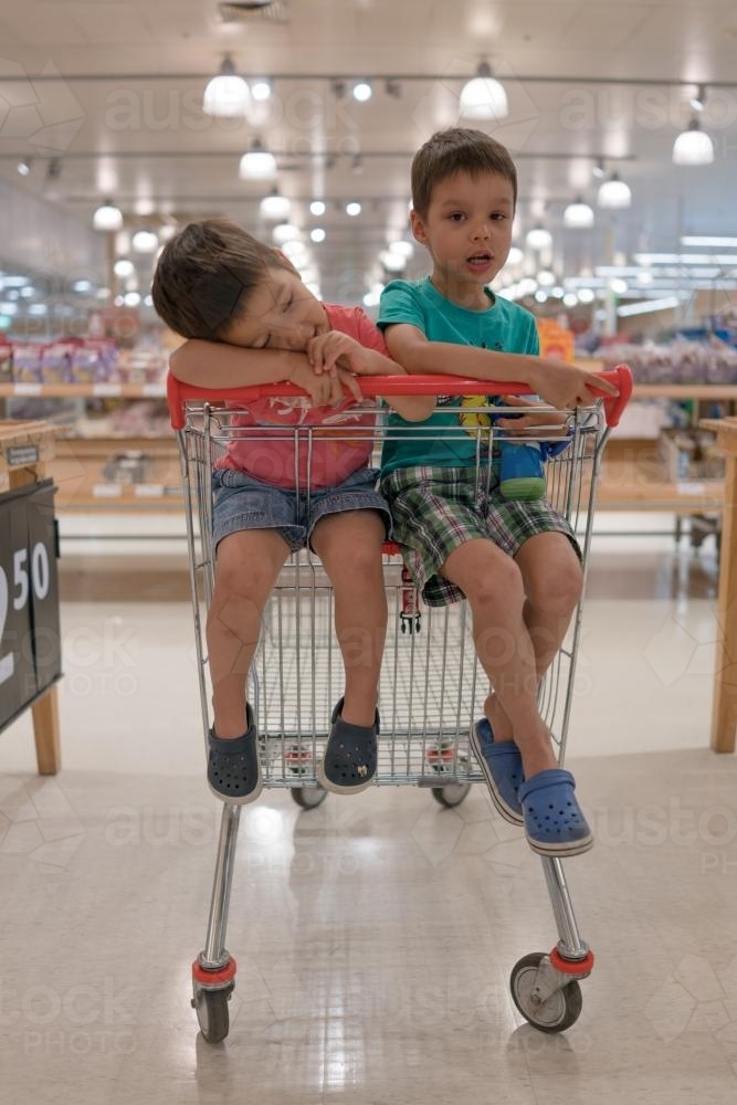Two mixed race brothers sit bored waiting in a supermarket shopping trolley - Australian Stock Image