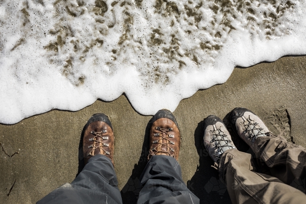 Two pairs of hiking boots on sandy beach with whitewash - Australian Stock Image