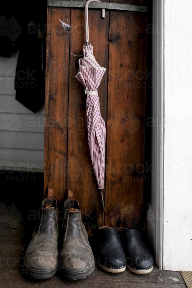 Two pairs of shoes lined up under a pink umbrella hanging inside doorway - Australian Stock Image