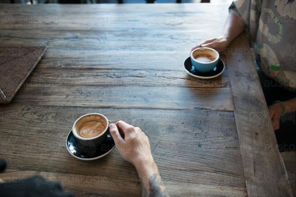 Two people drinking coffee at a wooden table - Australian Stock Image