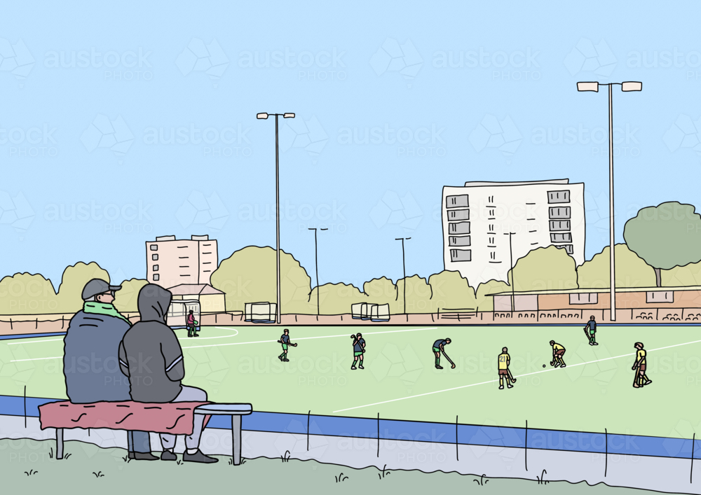 Two people rugged up to watch winter hockey game from sidelines - Australian Stock Image