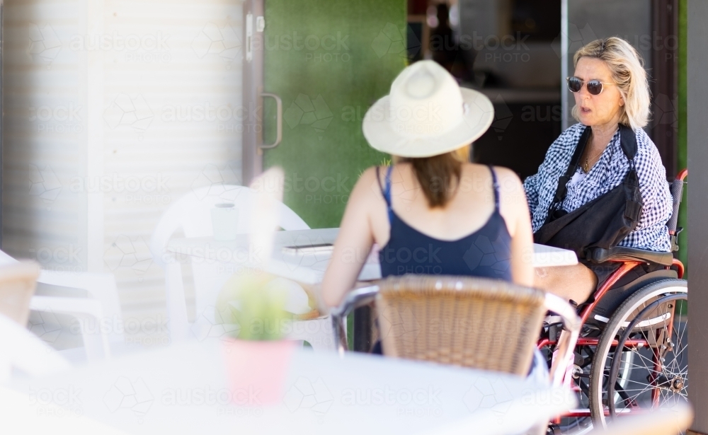 two people sitting at a cafe with one woman in a wheelchair - Australian Stock Image